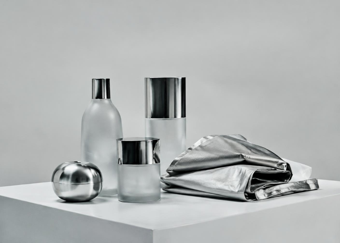 Chrome and frosted glass objects beside folded silver fabric